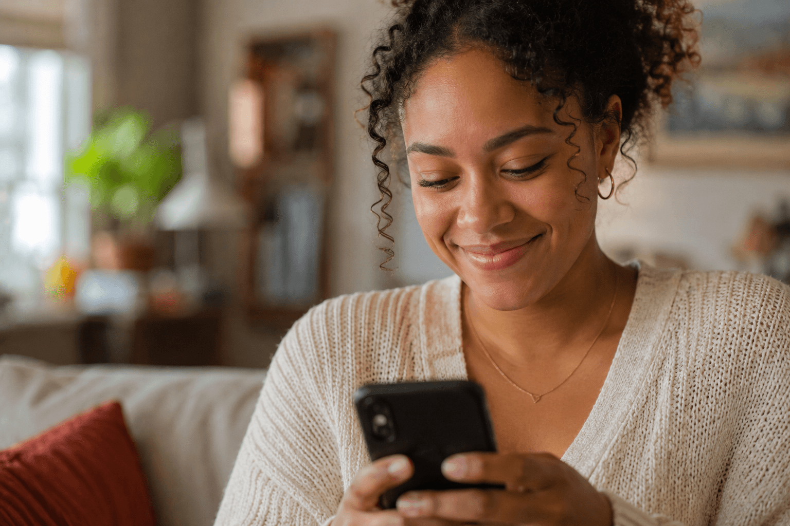A young woman smiling warmly at her phone as she sets up her family's newsletter