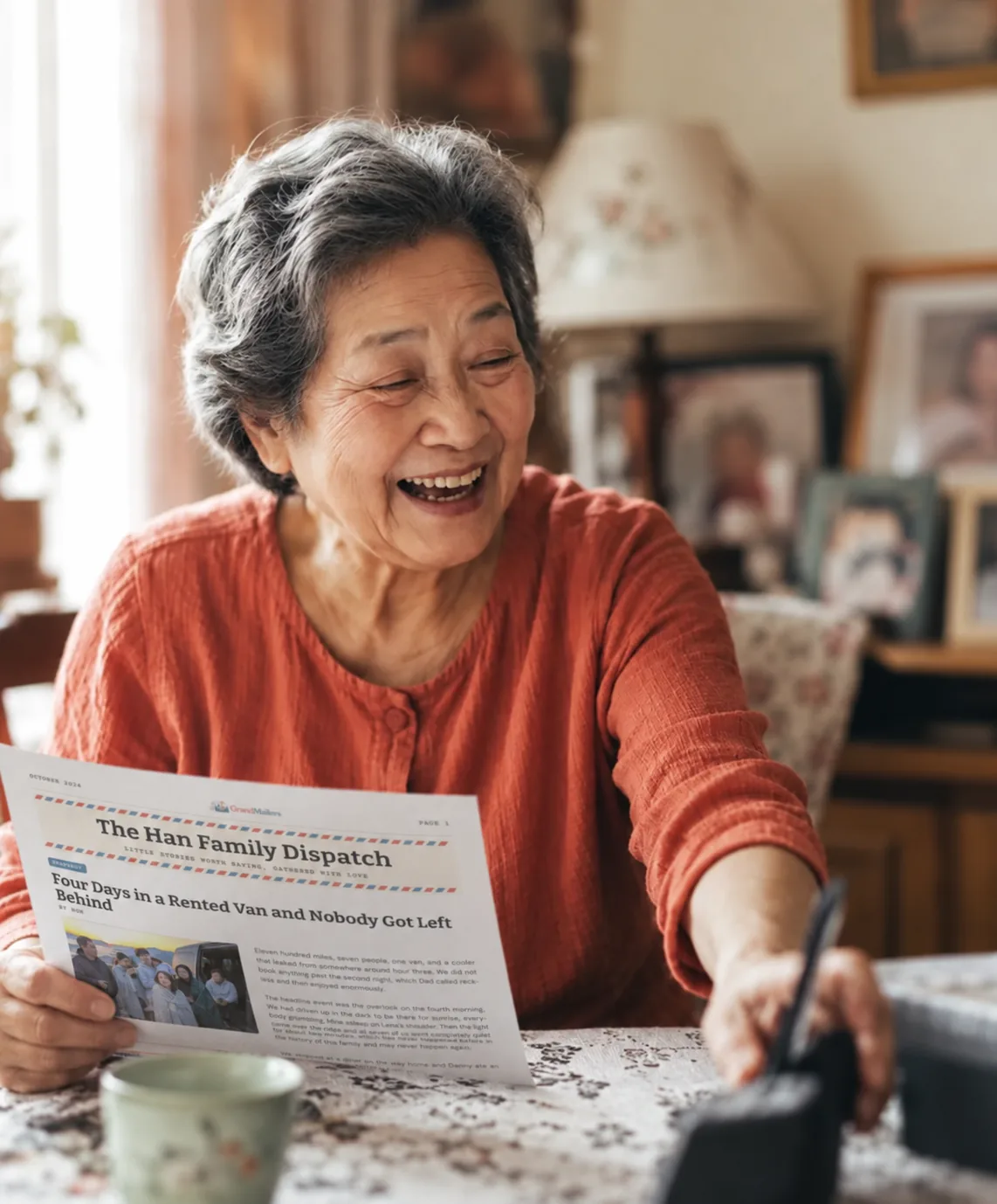 A grandmother laughing as she reads her family’s printed newsletter at her kitchen table